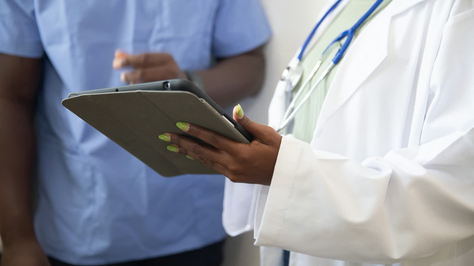 A doctor holding a tablet while talking with a colleague in a clinic
