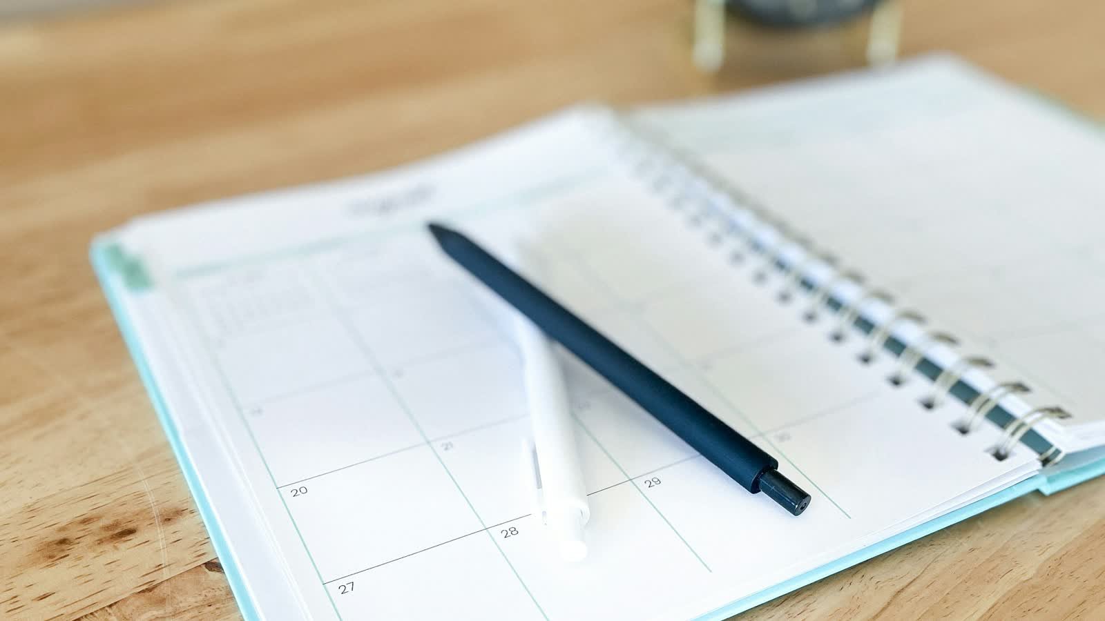 An open weekly planner with a pen resting on a wooden desk