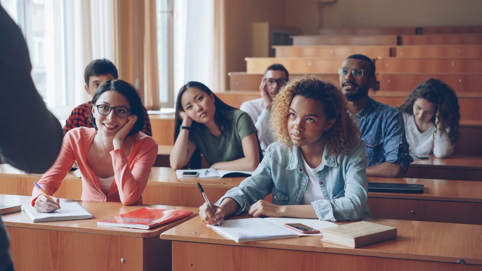 Students seated at desks in a university lecture hall taking notes