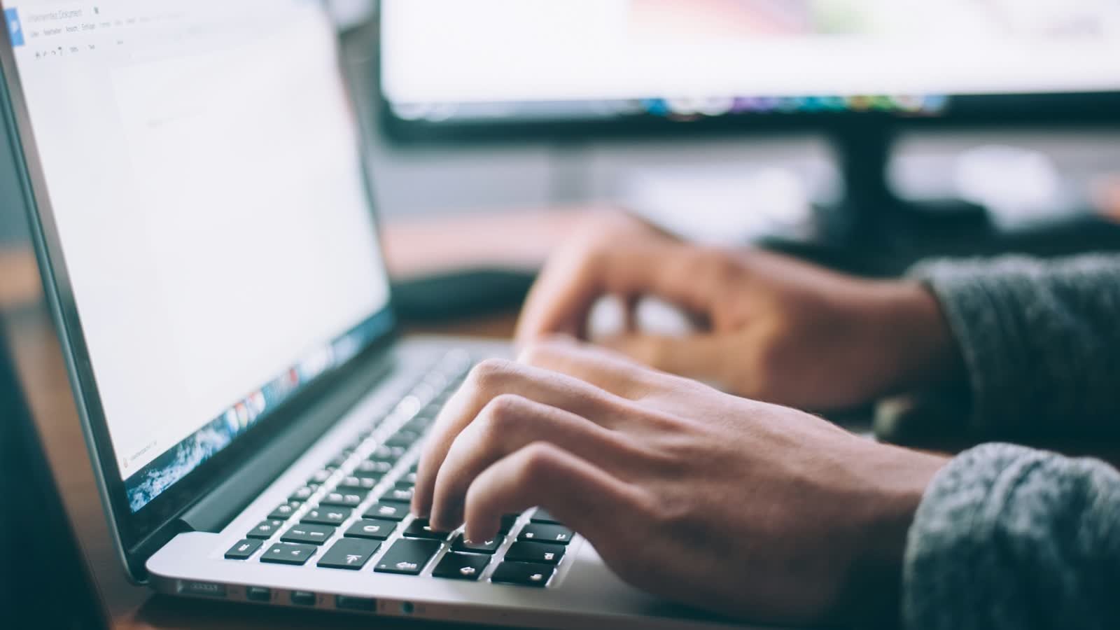 Close-up of hands typing on a laptop keyboard at a desk